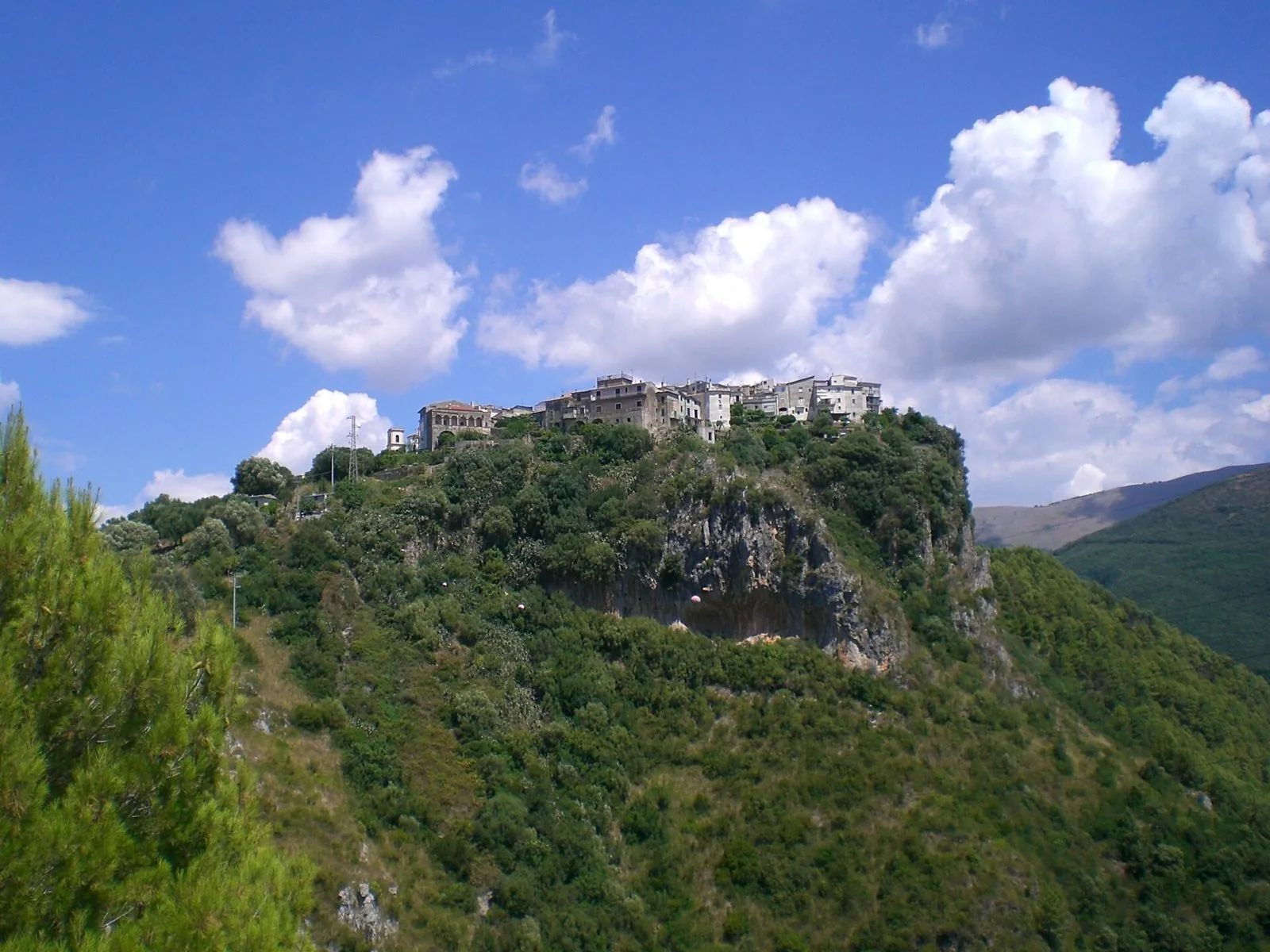 Il borgo di Camerota arroccato in cima a un rilievo verde, con le case in pietra contro un cielo azzurro con nuvole