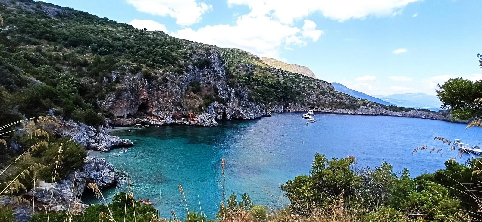 La baia di Porto Infreschi vista dall'alto tra la macchia mediterranea, con acqua turchese, scogliere e barche ancorate